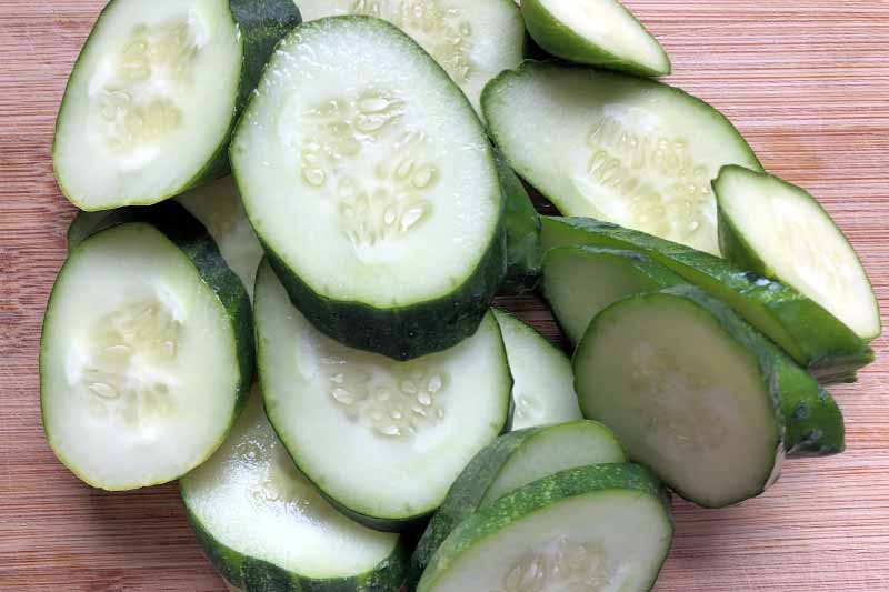 Horizontal closeup closely cropped overhead image of cucumber slices on an blonde wood surface.