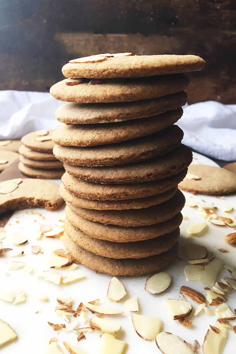 Vertical image of a tall stack of thin brown cookies surrounded by sliced almonds.