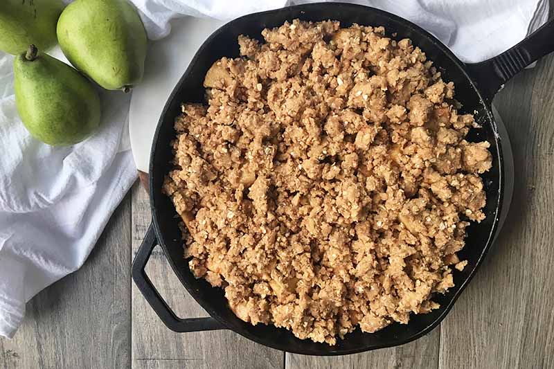 Horizontal image of a cast iron skillet with an oat crumble mixture spread on top.