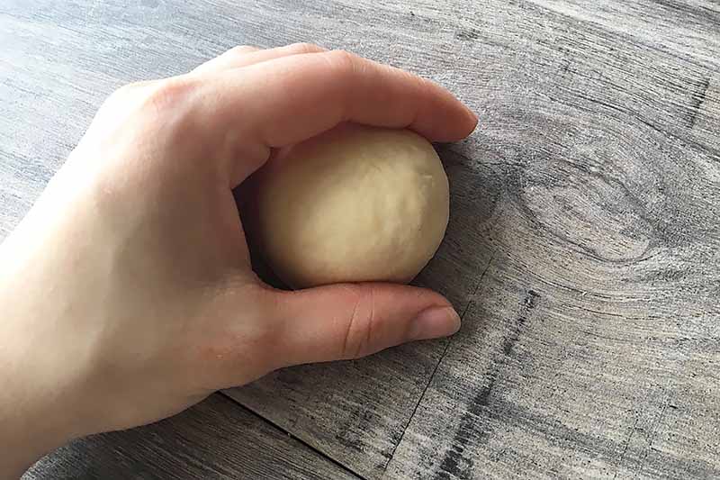 Horizontal image of a hand shaping a round ball of dough.