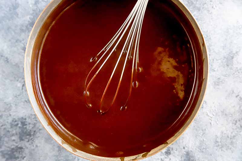 Horizontal image of a whisk in a pot with a dark brown liquid mixture.
