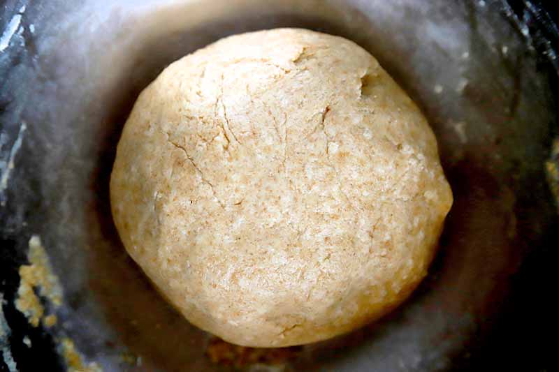 Horizontal overhead image of a ball of risen dough, in a stainless steel bowl.