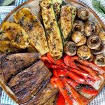 Horizontal top-down image of a platter with assorted grilled summer produce.