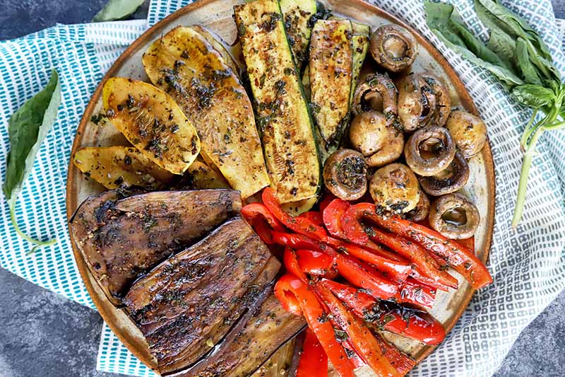 Horizontal top-down image of a platter with assorted grilled summer produce.