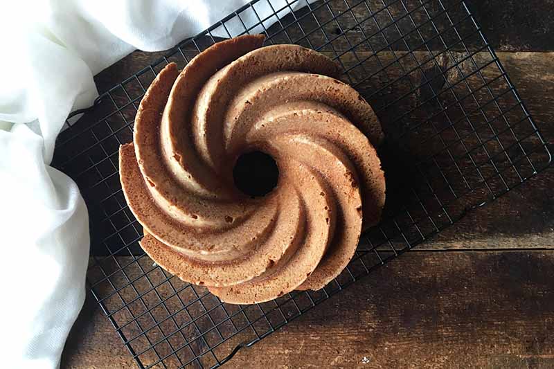 Horizontal image of a bundt on a cooling rack on a wooden surface.