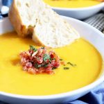 Horizontal image of a bowl of butternut squash soup with bacon garnish.
