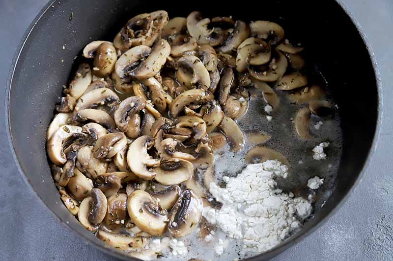 Horizontal image of sliced button mushrooms with liquid and a pile of flour.
