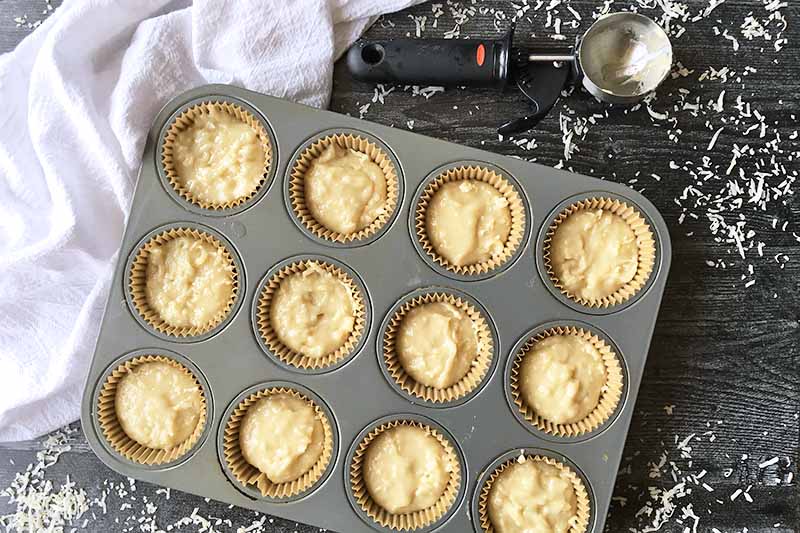Horizontal image of a muffin tin with each cup lined and filled with a light yellow batter.