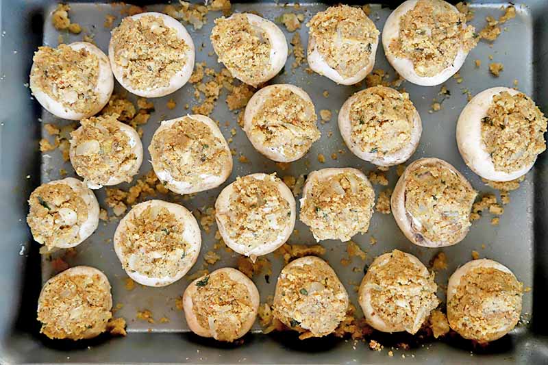 Horizontal image of stuffed unbaked mushrooms in a pan.