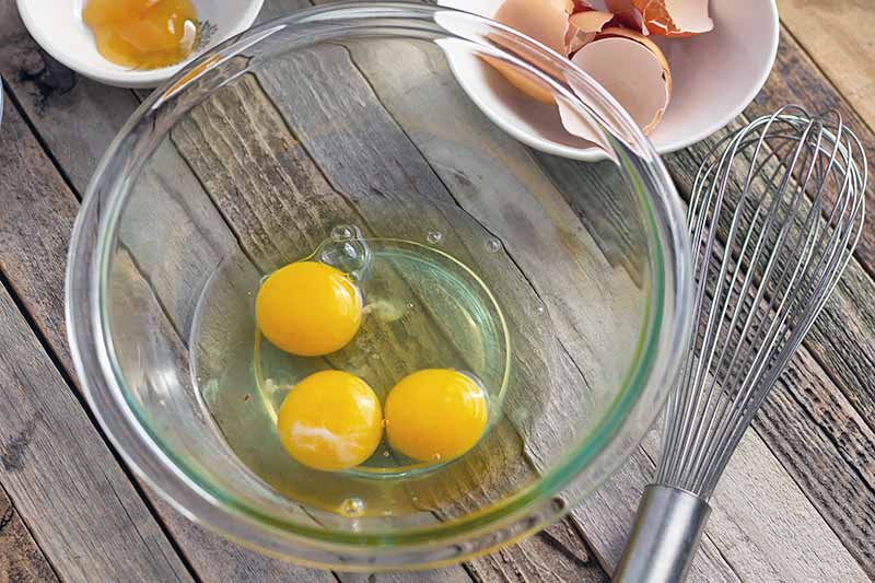 Horizontal image of three cracked eggs in a glass bowl.