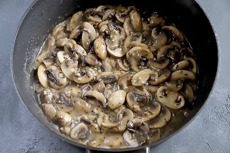 Horizontal image of mushrooms in a thickened gravy in a pot.