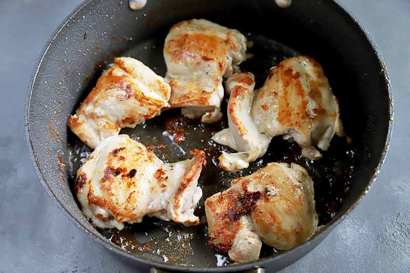 Horizontal image of a pan with seared poultry thighs.