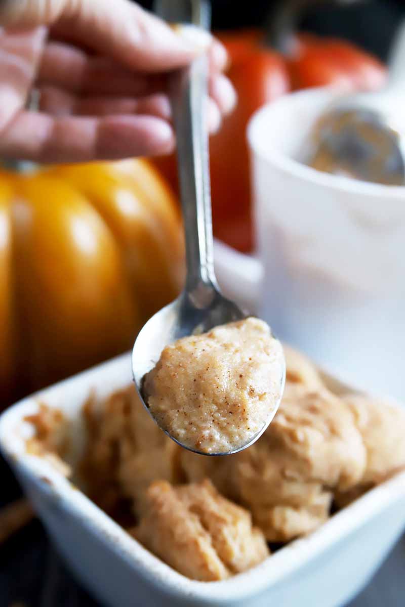 Vertical close-up image of a metal spoon holding a spoonful of a spiced pumpkin ice cream dessert, in front of fall decorations.