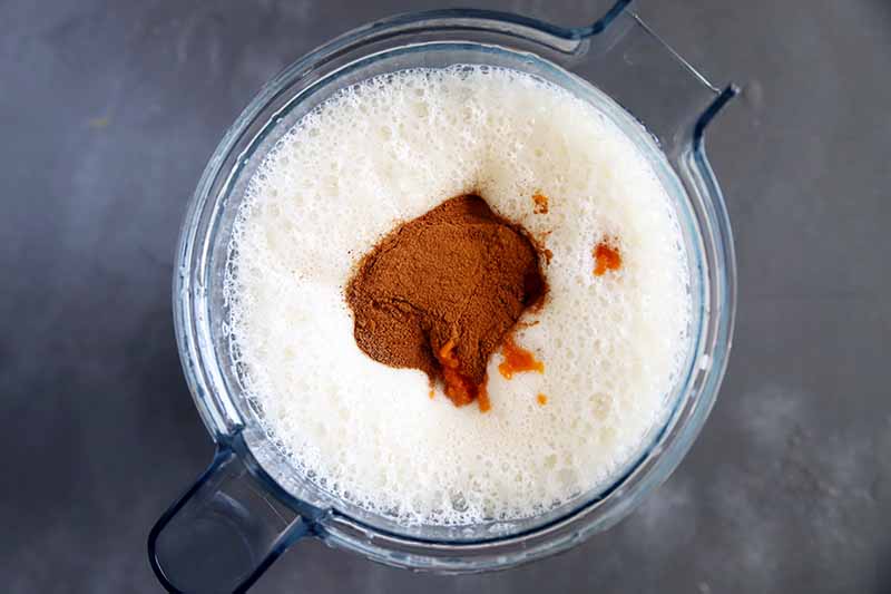 Horizontal image of squash puree on top of frothy milk in a blender.