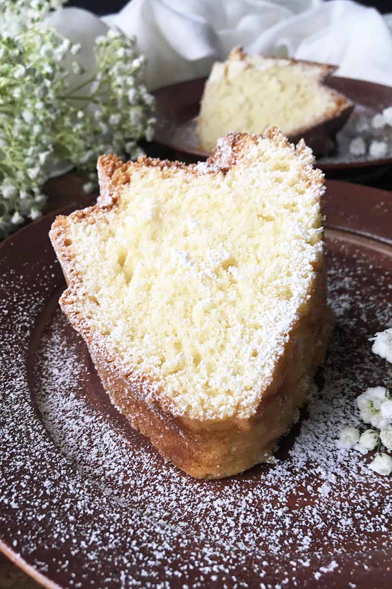 Vertical close-up image of slices of cake on brown plates dusted with confectioners' sugar.