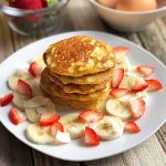 Horizontal image of a stack of small pancakes on a white plate with fresh fruit.