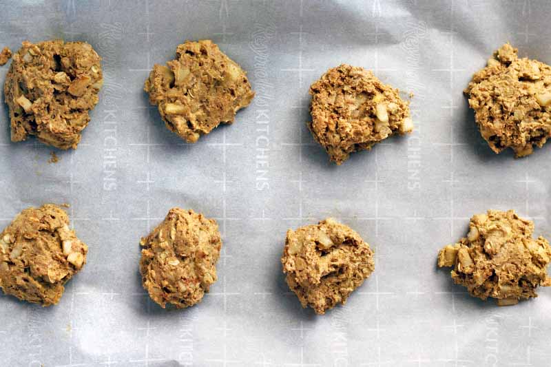 Horizontal overhead image of eight portions of cookie dough arranged in two rows on a piece of white parchment paper.