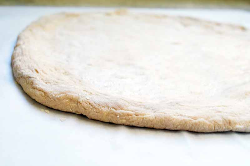Horizontal close-up image of a rolled out round of pizza dough on a lightly floured surface.