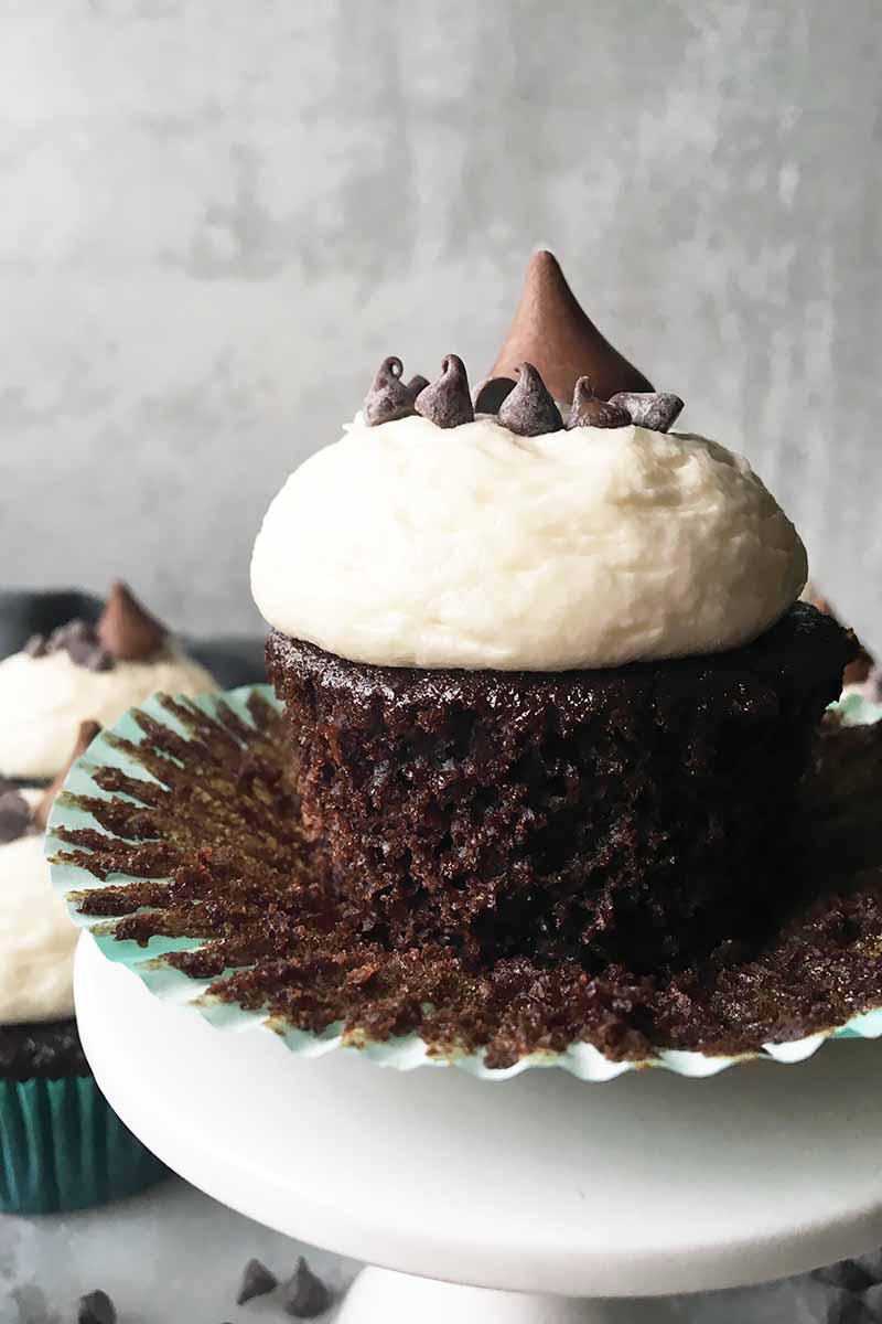 Vertical image of a liner peeled away from a chocolate cupcake with vanilla frosting. 