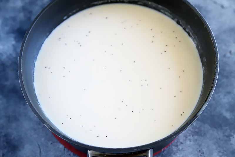 Horizontal image of a cream mixture sprinkled with black pepper specks in a black pot.