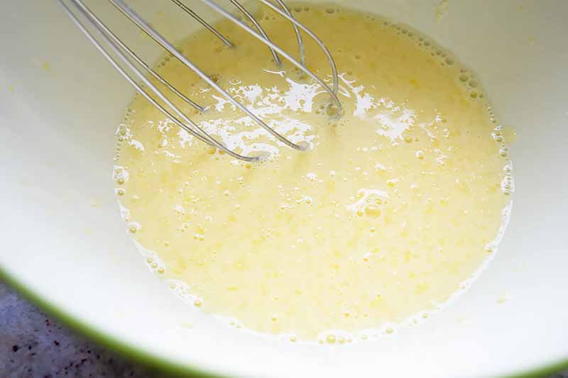 Horizontal image of a whisk in a light yellow batter.