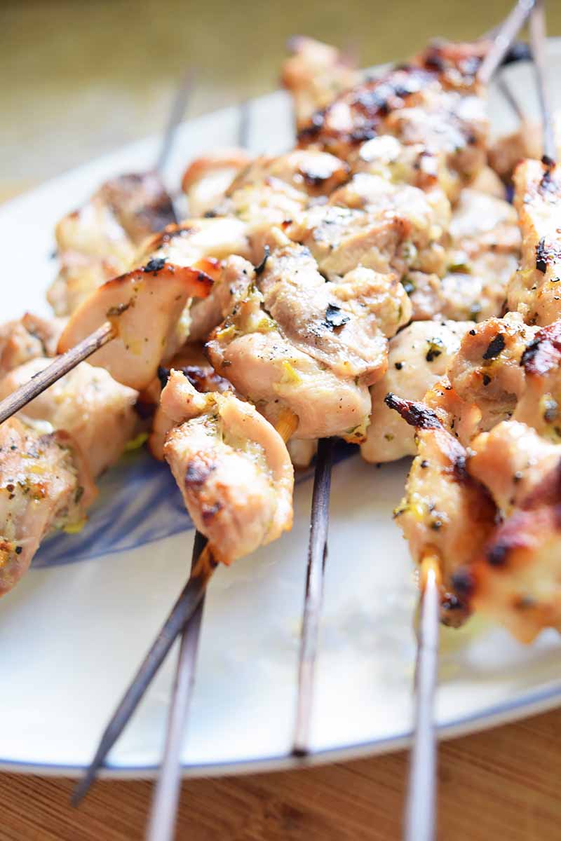 Vertical image of grilled marinated chicken on bamboo skewers.