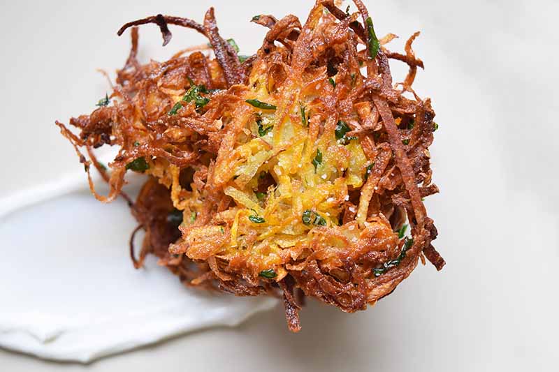 Overhead horizontal image of a crispy fried latke with sour cream, on an off-white surface.