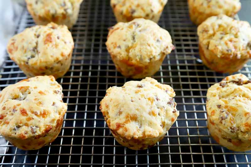 Horizontal image of homemade sausage and cheese biscuits that were baked in a muffin tin, on a wire cooling rack arranged in three rows.
