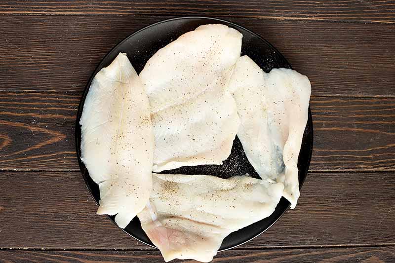 Horizontal image of uncooked fish fillets seasoned with salt and pepper.