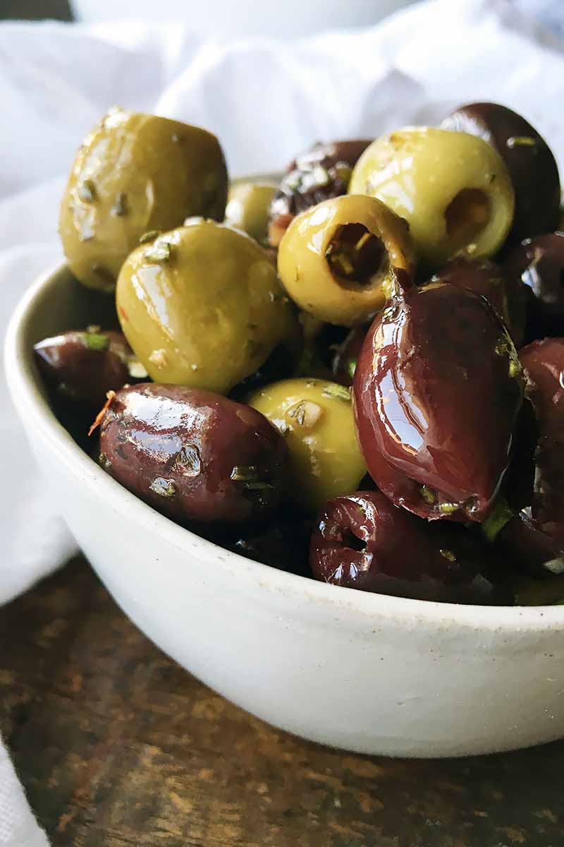 Vertical close-up image of a white bowl with flavored olives.