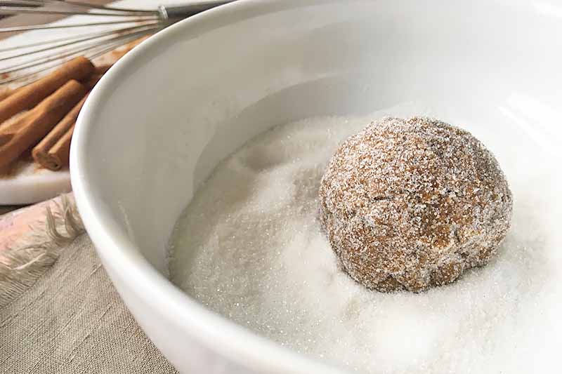 Horizontal image of a bowl of sugar with a dough ball on top, coated in the mixture.