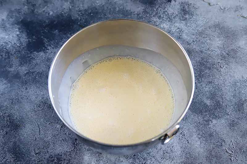 Horizontal image of a frothy, light yellow liquid in a metal bowl.