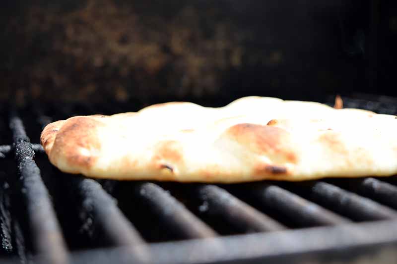 Horizontal image of a piece of pita bread on the grates of a grill.