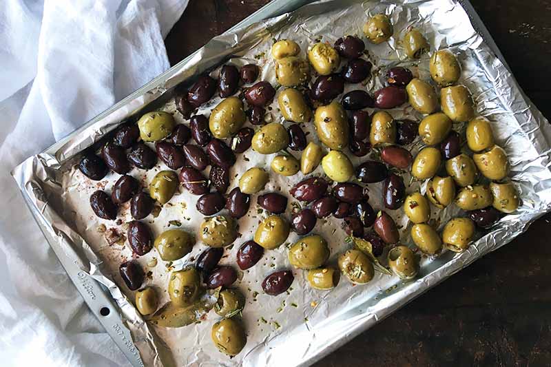 Horizontal image of a sheet pan with assorted roasted olives.