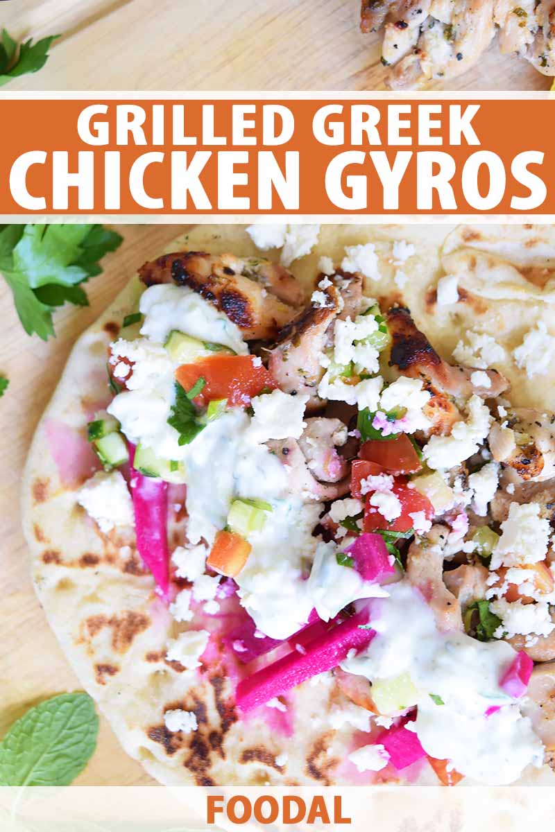Vertical overhead image of an open-faced chicken gyro with yogurt sauce, cucumber tomato salad, pickled beets and turnips, and crumbled feta, with sprigs of fresh parsley on a wooden cutting board, printed with orange and white text near the top and at the bottom of the frame.