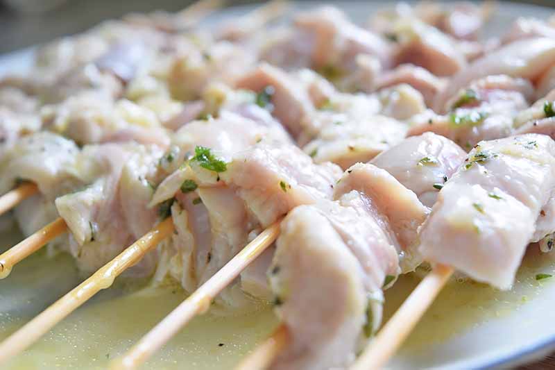 Horizontal close-up image of raw chopped chicken thigh meat on wooden skewers.