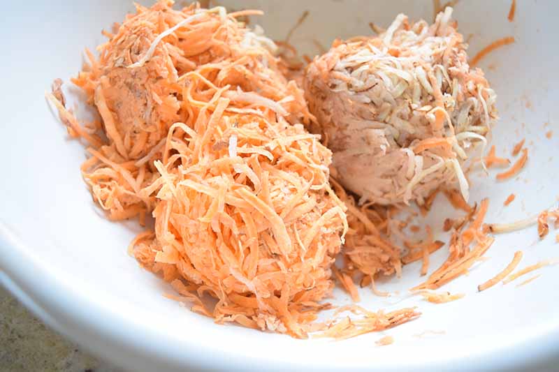 Shredded sweet potato mixed with flour and egg, and formed into patties, in a white bowl.