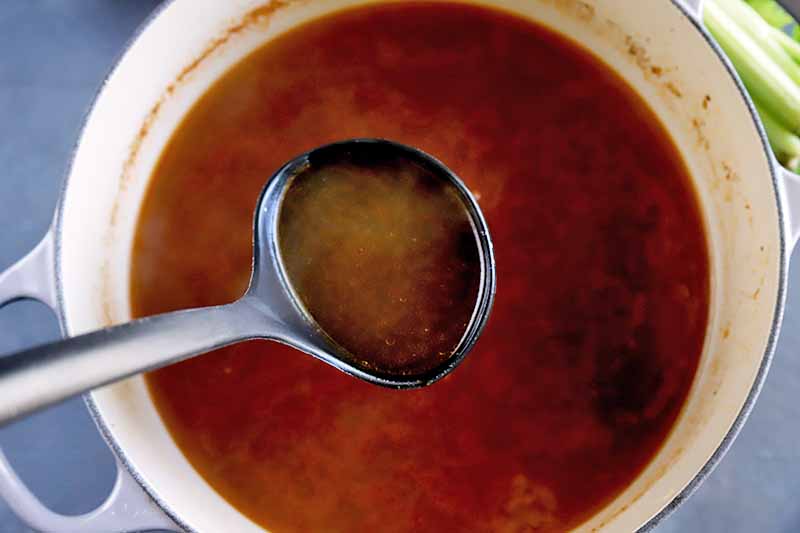Horizontal image of a ladle in a pot full of a deep red liquid.