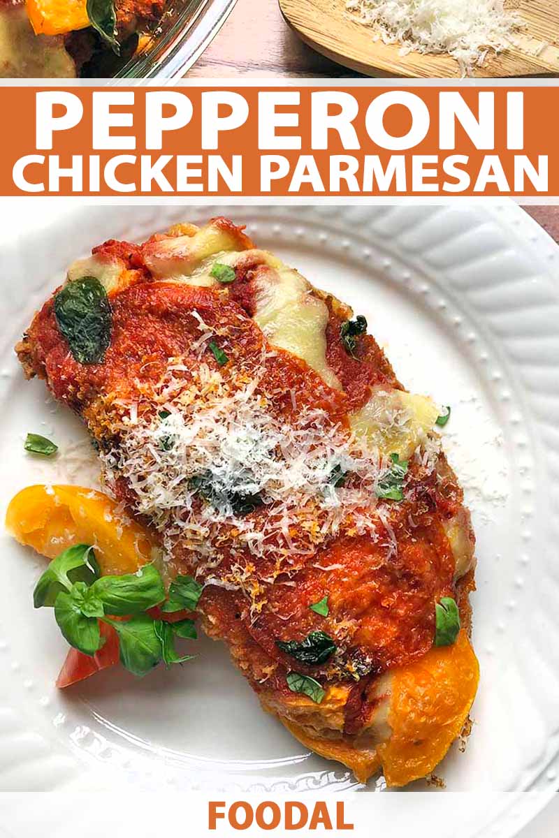 Vertical image of chicken parmesan on a white plate with a decorative fluted edge, garnished with red and yellow tomato slices, fresh basil, and grated cheese, on a table with a wooden spoon, printed with orange and white text in the top third and at the bottom of the frame.