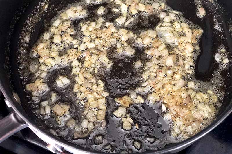 Closely cropped overhead image of a nonstick pan of onions sauteeing in oil.