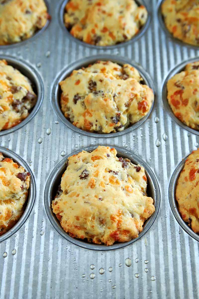 Vertical oblique overhead image of a metal muffin tin filled with nine freshly baked sausage cheese biscuits.