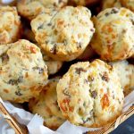 Horizontal closely cropped oblique overhead image of a basket lined with parchment paper and filled with sausage cheese biscuits, on a blue-gray surface topped partially with more paper.