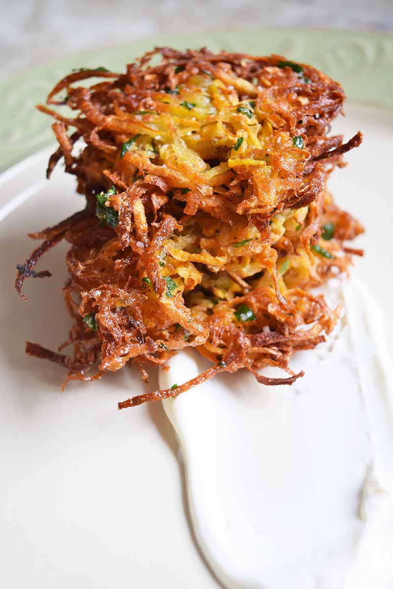 Vertical image of a stack of crispy shredded potato patties that have been fried in oil, on a white surface.