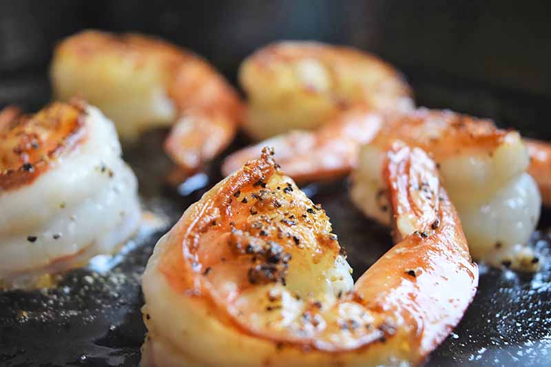 Horizontal image of cooking seasoned shrimp in a pan.