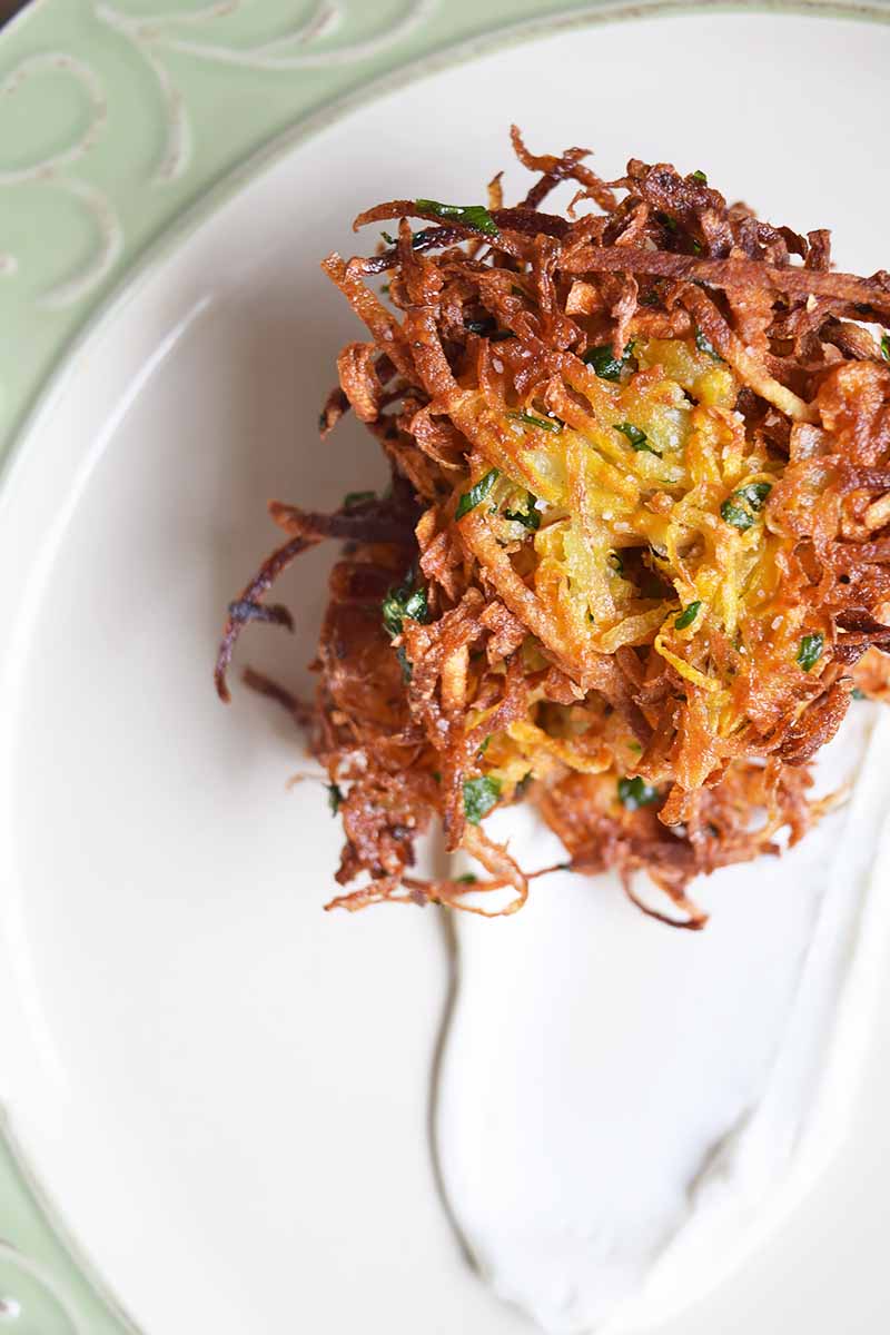 Overhead image of a short stack of crispy potato latkes on a white plate with a smear of sour cream, on a white plate with a pastel green rim.