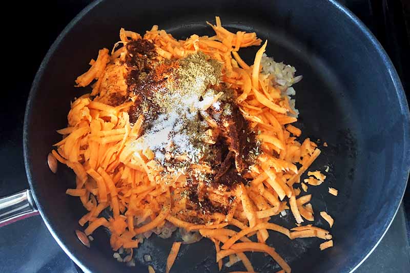 Overhead horizontal image of a nonstick frying pan of shredded sweet potato and spices.