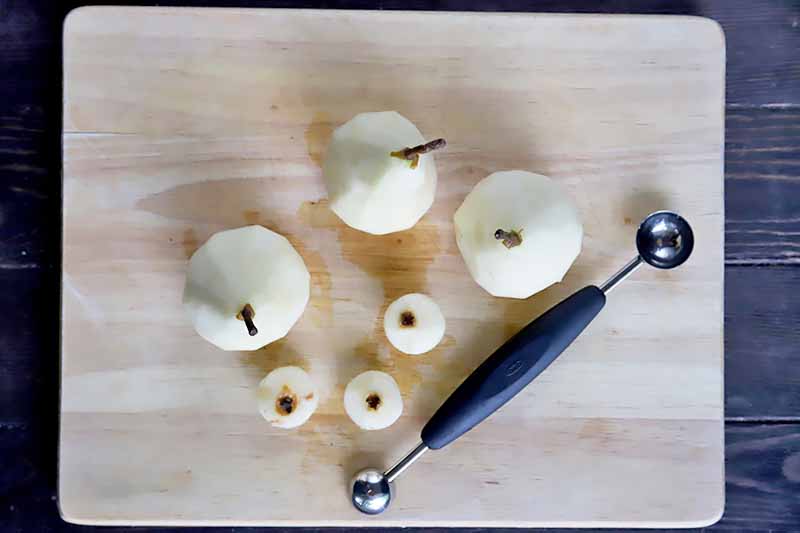 Horizontal image of peeled whole fresh pears with the cores removed next a metal melon baller.