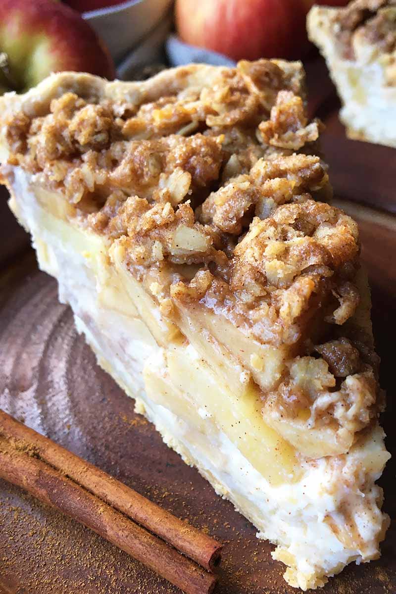 Vertical close-up image of an apple cream cheese streusel pie on a brown plate with a cinnamon stick.