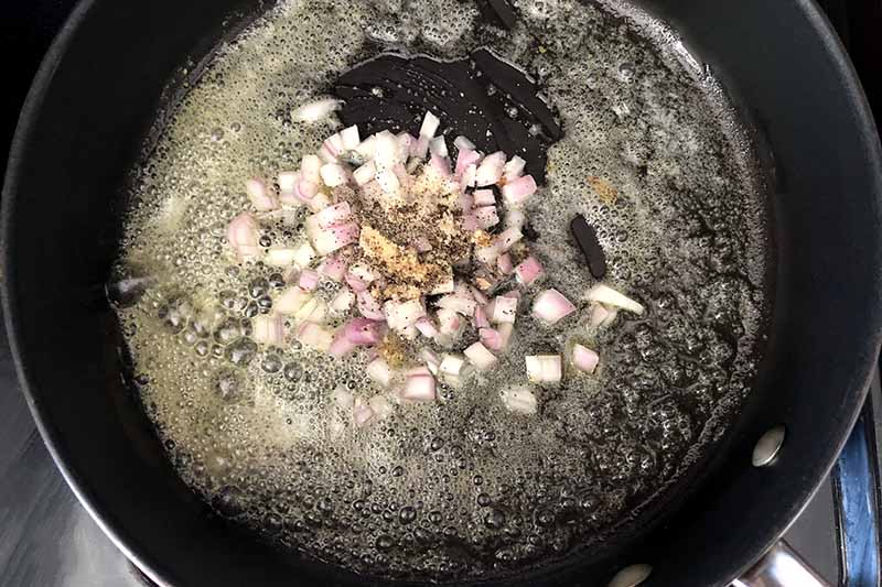 Horizontal overhead image of a nonstick frying pan of butter, oil, chopped onion, salt, pepper, ginger, and garlic powder.