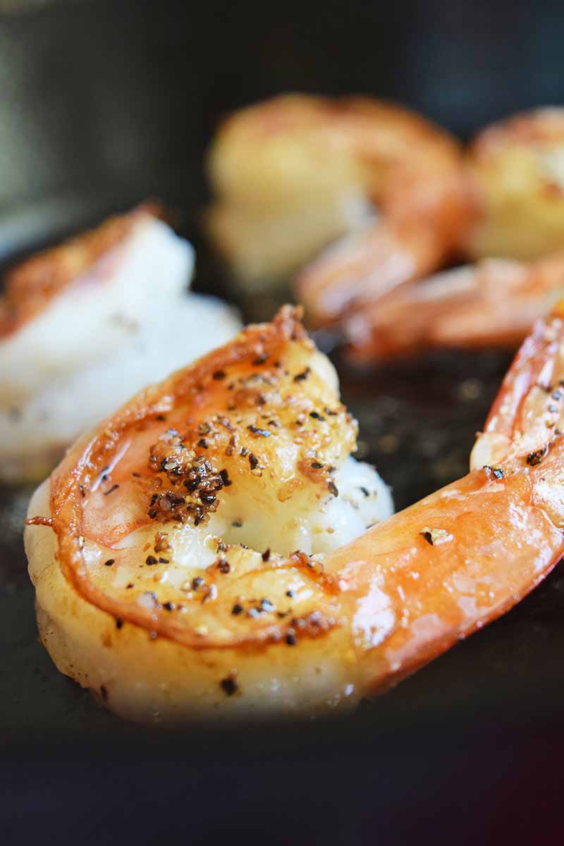 Vertical image of whole shrimp cooking in a pan.